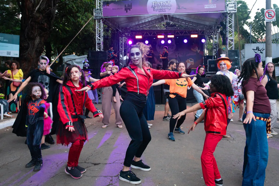 Instrutora de jaqueta vermelha e crianças fantasiadas dançando a coreografia de Thriller diante do palco do Festival Halloween Moema