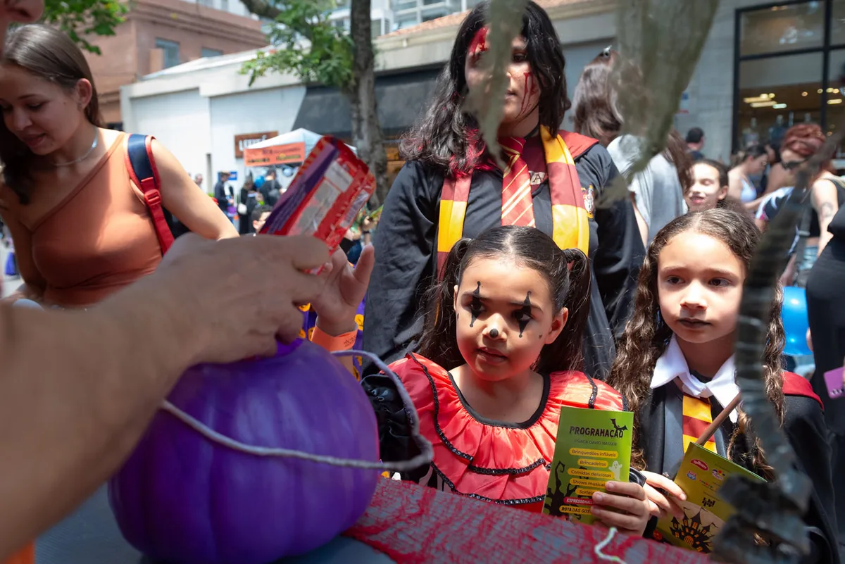 Criança fantasiada recebendo doces em um baldinho durante a Trilha do Halloween